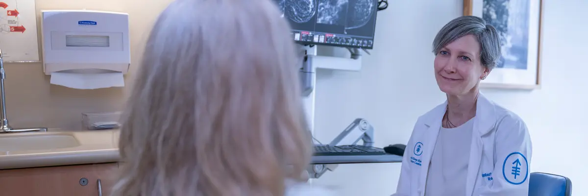 Radiologist Dr. Kimberly N. Feigin is in an exam room with a patient, with breast scans on a monitor behind her.