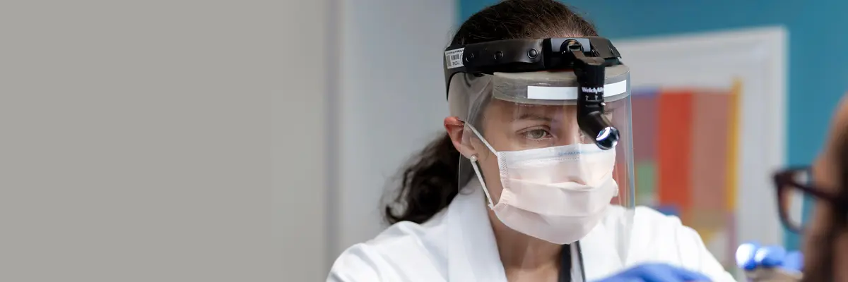 Head and neck surgeon Dr. Valeria Silva Merea, who treats people with voice, airway, and swallowing problems, wears a medical headlamp to examine a patient. 