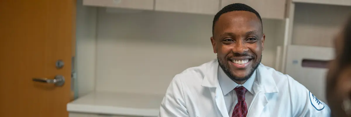 Genitourinary medical oncologist Dr. Emmett Wynter, wearing a white doctors’ coat, smiles as he talks with his patient in an MSK exam room. 