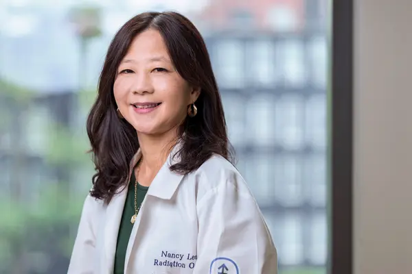 Radiation oncologist Dr. Nancy Lee, smiling, is pictured at MSK wearing a white doctors’ coat. 