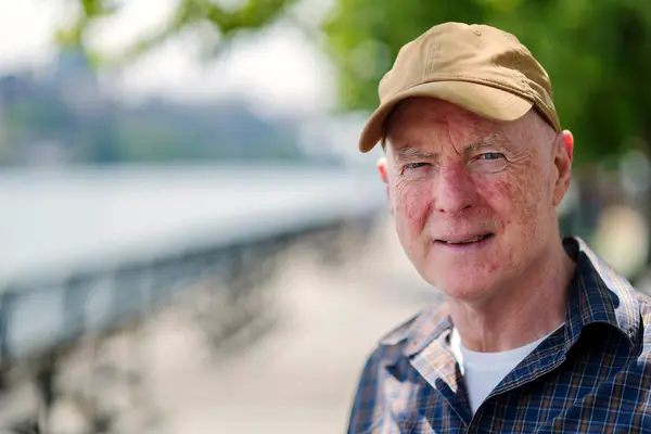 Rowing coach James Mangan, wearing a hat, is standing by a river.  