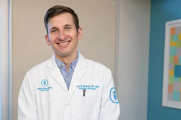 Radiation oncologist Dr. Sean McBride, wearing a white doctor’s coat, stands in a hallway at MSK in NYC. 