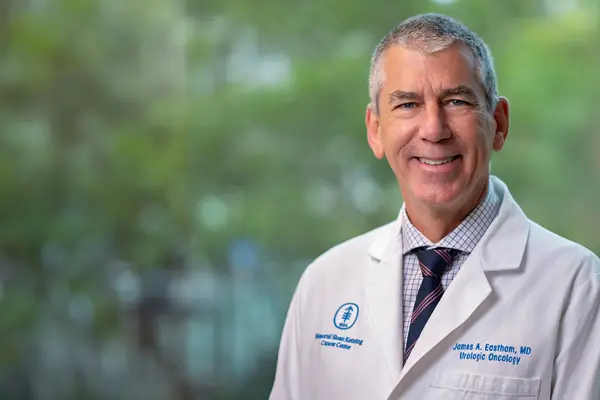 Dr. Eastham, wearing a white doctors’ coat, in front of a blurred background of trees. 