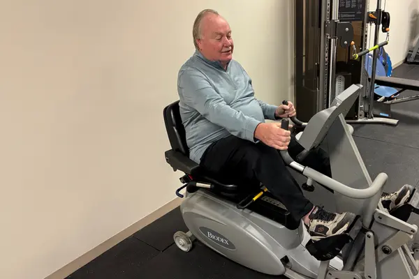 Robert is wearing exercise clothing and using a recumbent stationary exercise bike. 