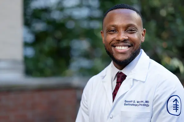  Dr. Wynter, wearing a white doctors’ coat and smiling, is standing outside MSK. 
