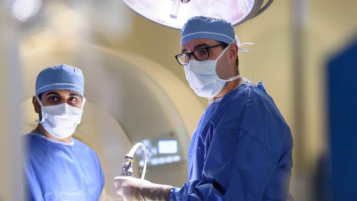 Head and neck surgeon Dr. Marc A. Cohen is in an MSK surgery suite with another surgery team member, both masked and in surgery scrubs. 
