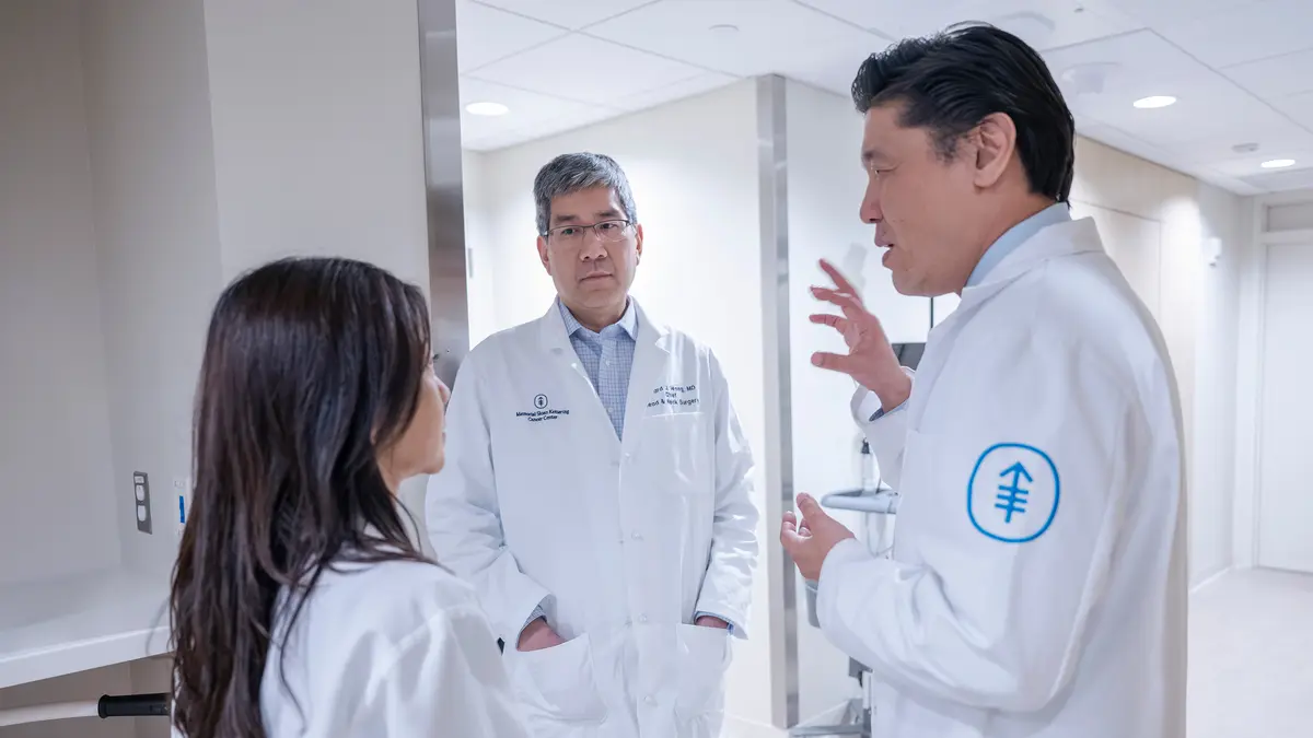 Dr. Nancy Lee, Dr. Richard Wong, and Dr. Alan Ho talk in a hallway about patient care. 
