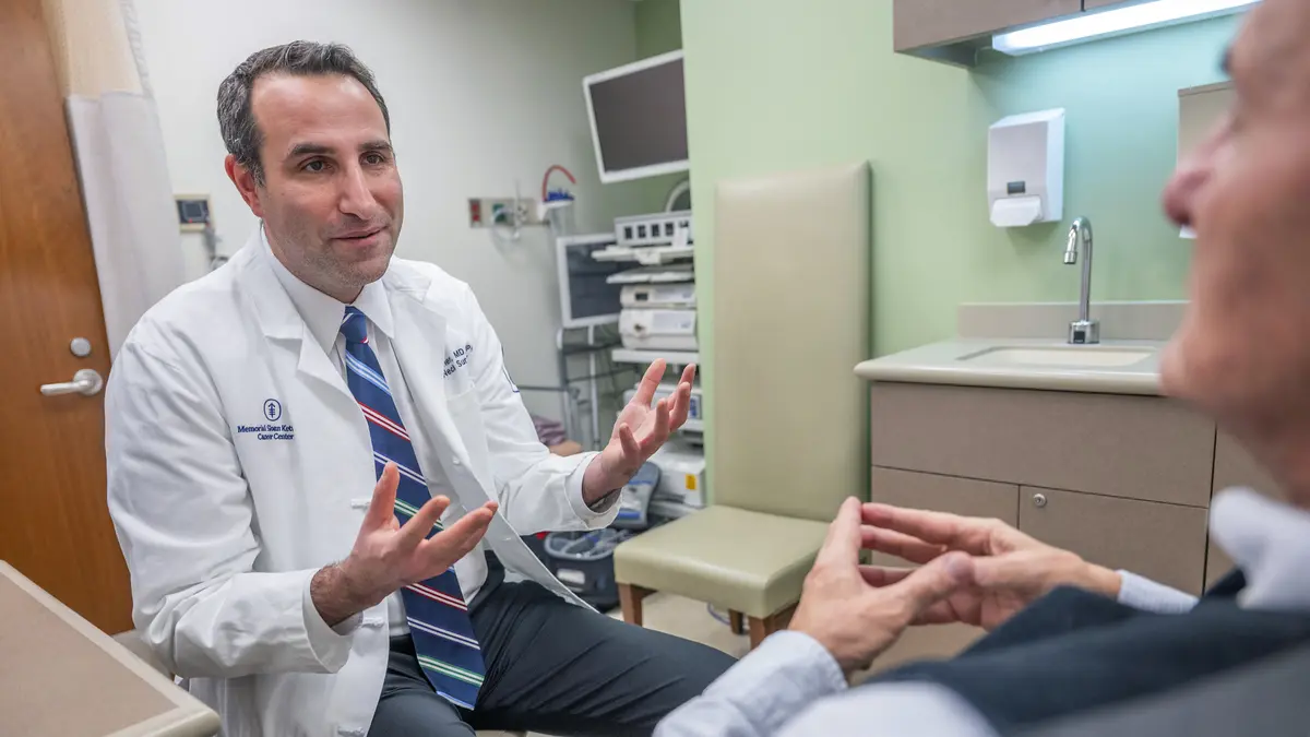 An MSK head and neck surgeon gestures with his hands as he talks with his patient in an exam room. 