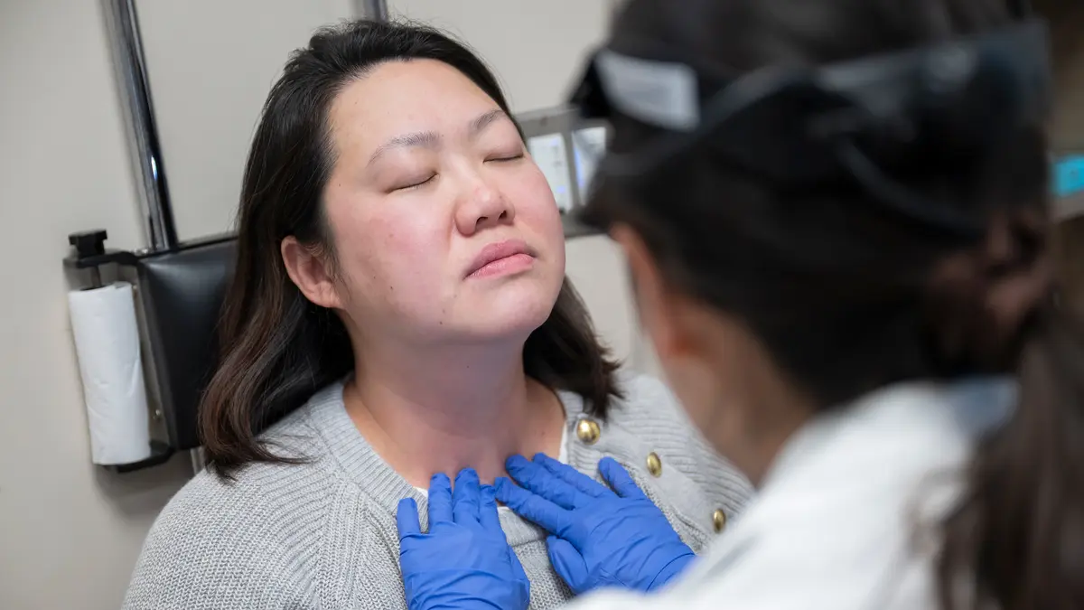 An MSK head and neck expert, wearing a headlamp, uses her gloved hands to examine her patient’s neck. 
