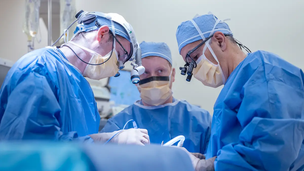 An MSK head and neck surgeon and 2 colleagues, all wearing surgical gear, during a surgery.