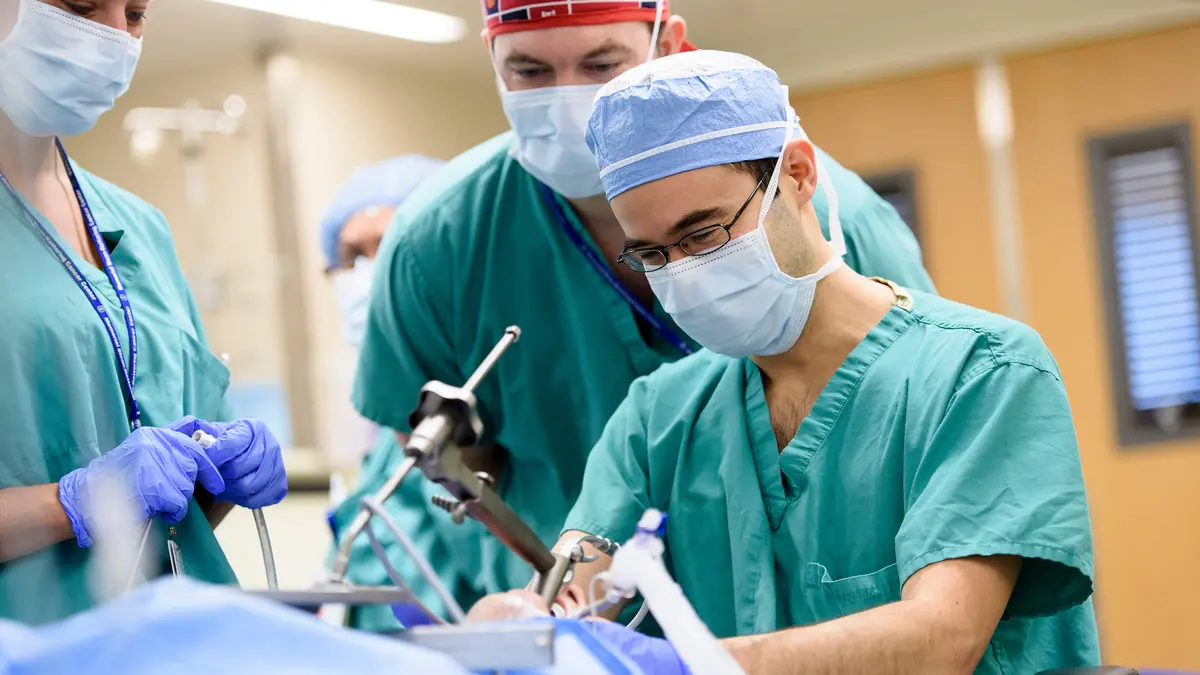 Three members of an MSK surgery team, wearing surgical scrubs, during a surgery. 