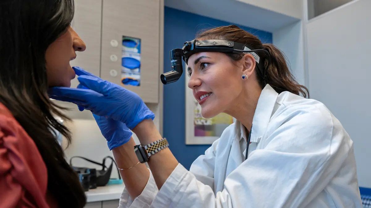 A nurse practitioner, wearing a headlamp, examines her patient’s mouth with gloved hands. 