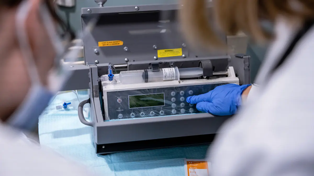 Two MSK care team members during a theranostics procedure, with one of them pressing a button on a machine with a gloved hand. 