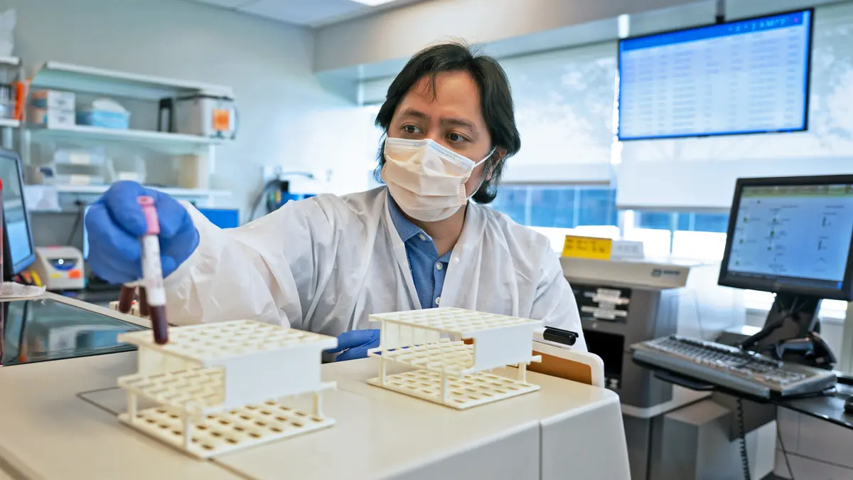 Inside an MSK lab, a technician in protective clothing puts a test tube into a specimen holder.  