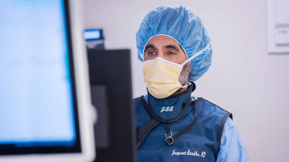 Urologic surgeon Dr. Jaspreet Sandhu, wearing surgical protection, looks at a monitor. 
