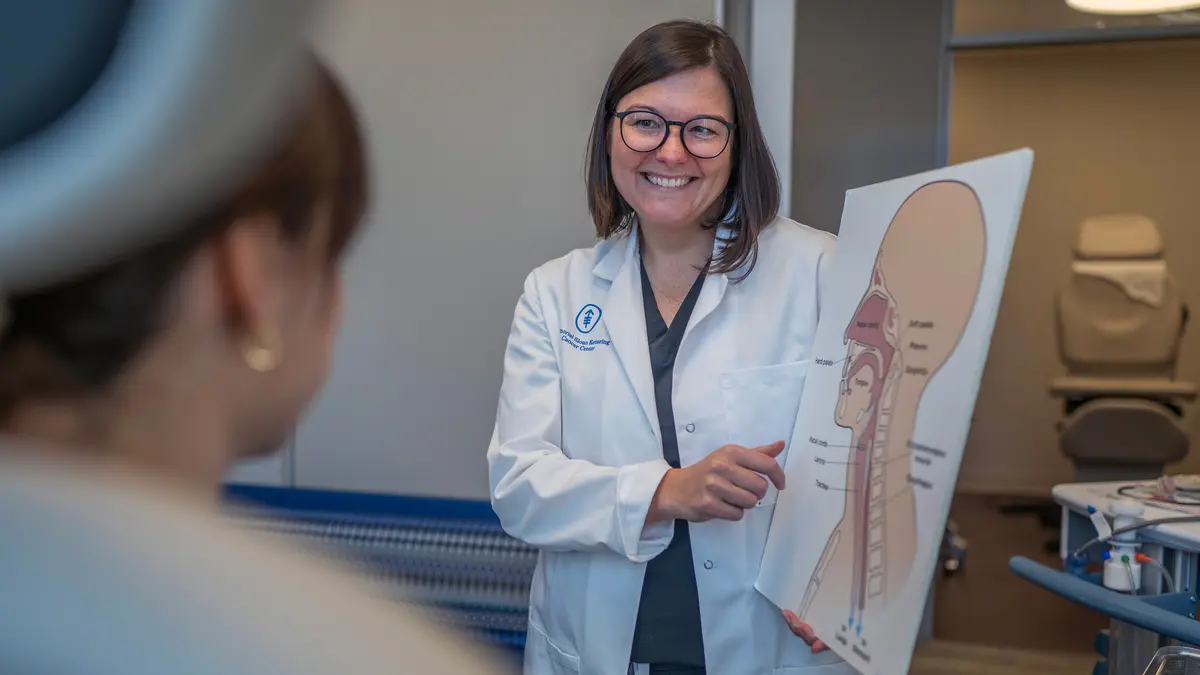 A speech pathologist holds a large illustration of the parts of the head and neck to show her patient. 