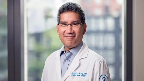 Dr. Wong, smiling and wearing a white coat, is at MSK in New York City. 