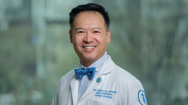 Kenny Lin, in a white coat and bow tie, is standing by a window at MSK.